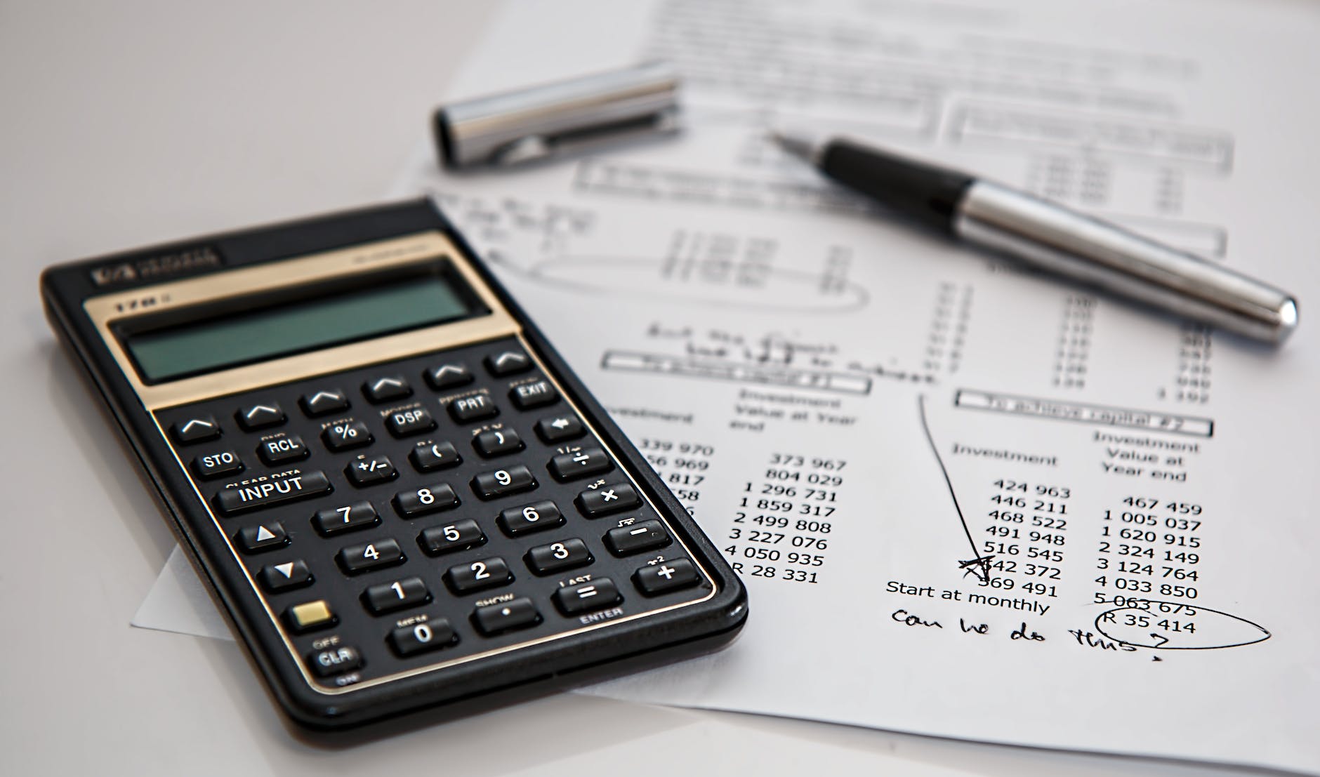 black calculator near ballpoint pen on white printed paper doing budgeting 